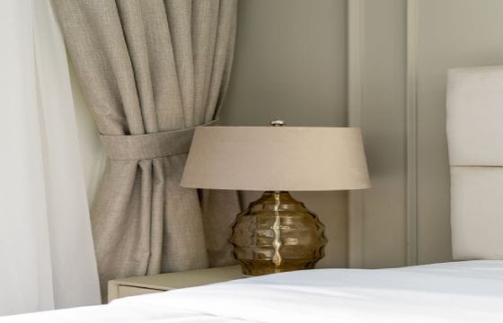 Beżowe zasłony i lampka nocna w eleganckiej sypialni